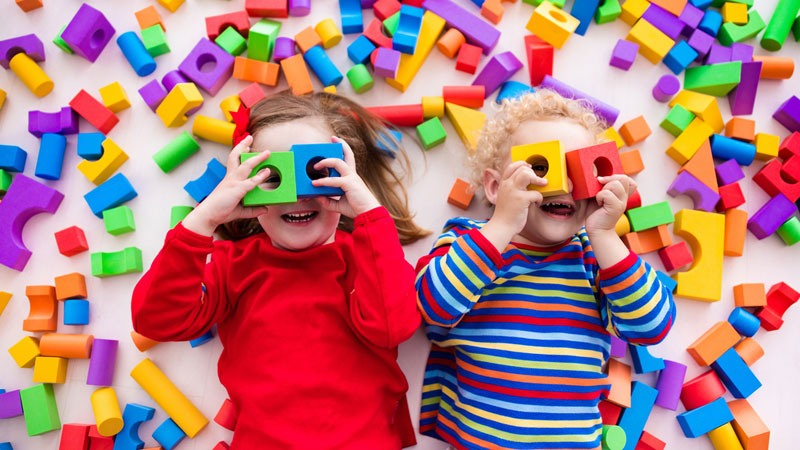 silly kids lying on the floor and looking through wood block holes