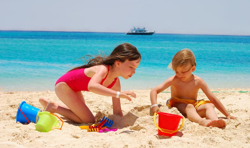 sister playing with little brother in the beach sand by the water