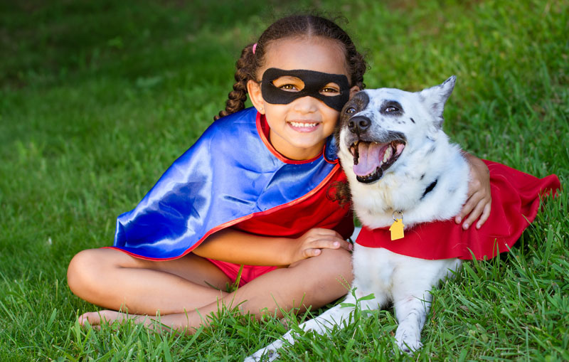 little girl dressed up as a superhero with her dog on the grass