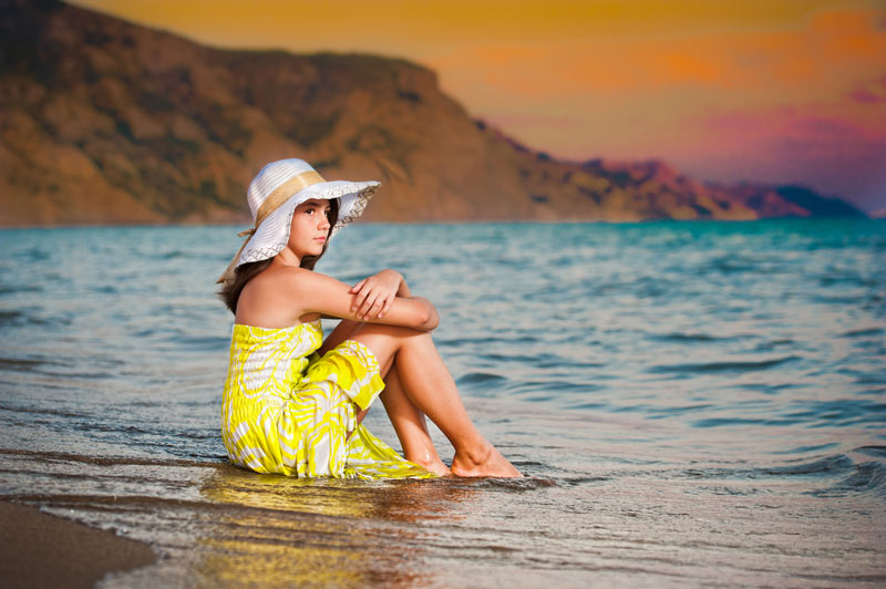 teen girl in yellow sundress sitting at waters edge