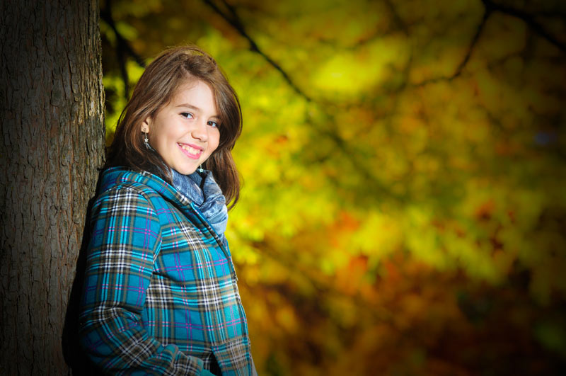 teen girl posing beside fall leaves on a tree
