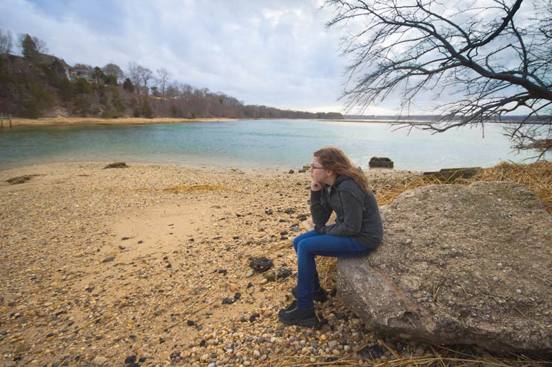 teen girl sitting on a rock next to the lake and contemplating