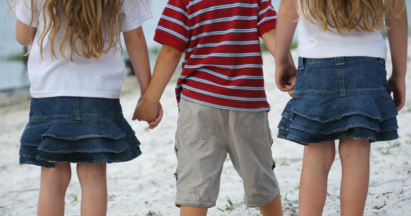 three siblings holding hands and viewed from behind