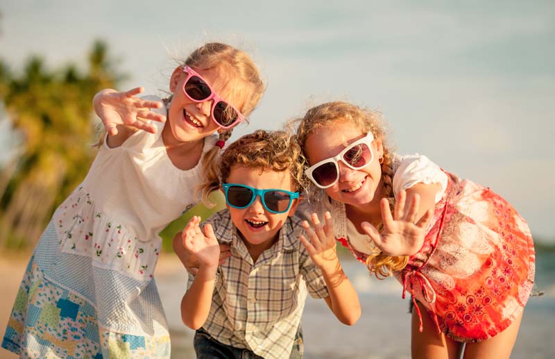 three young siblings with sunglasses posing outside happily for photo