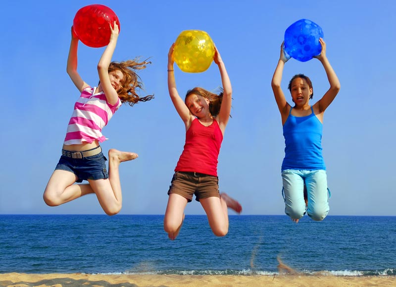 three young teen girls jumping on the beach while holding beachballs
