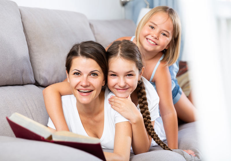 two young girls on mothers back listening to a book being read