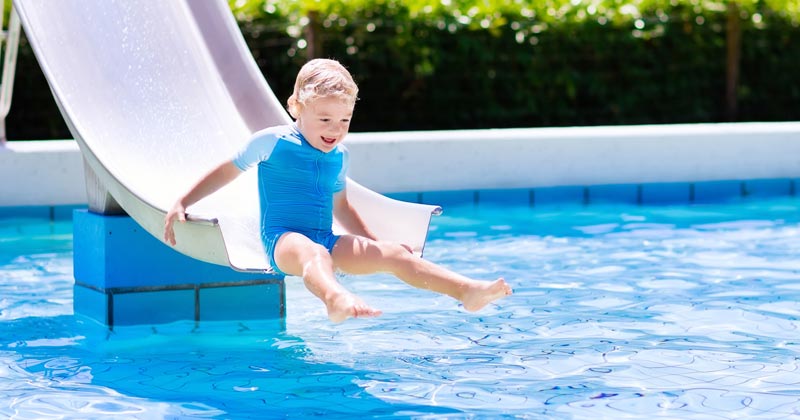 very young boy going down the slide into the pool