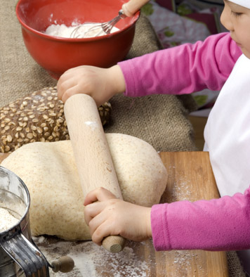 young baker girl rolling out bread dough