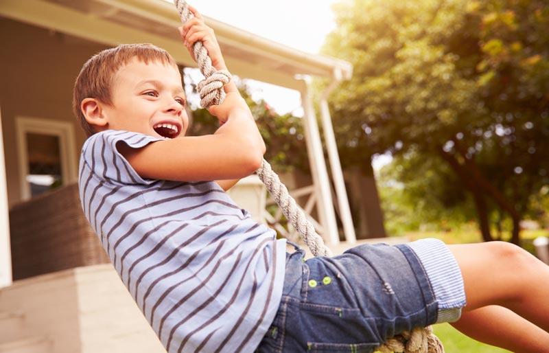 young boy swinging by a rope hanging from a tree in his backyard