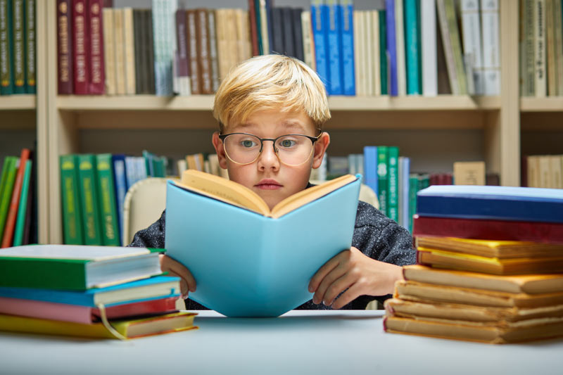 young boy with glasses reading book in the library