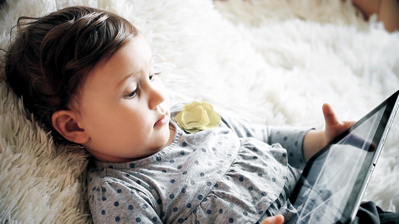 young child holding tablet while lying on bed