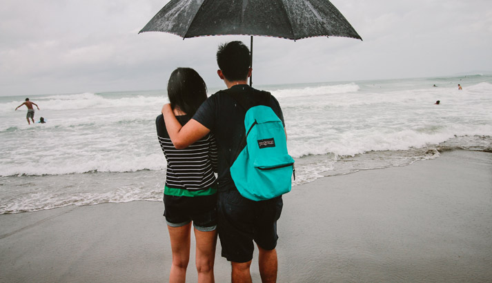 young couple holding an umbrella while at a rainy beach
