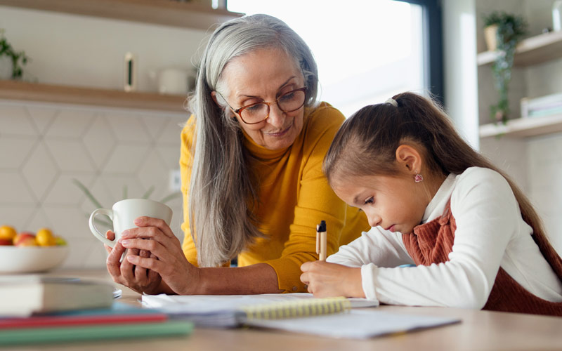 young girl doing her homework in the kitchen with her grandmother helping her