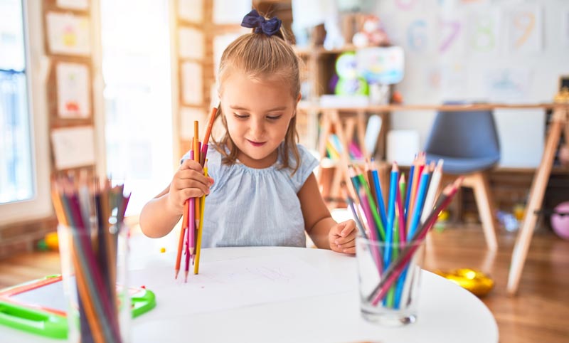 young girl doodling with a bunch of colored pencils on some paper
