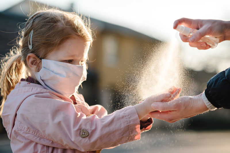 young girl wearing face mask getting her hands sprayed with sanitizer