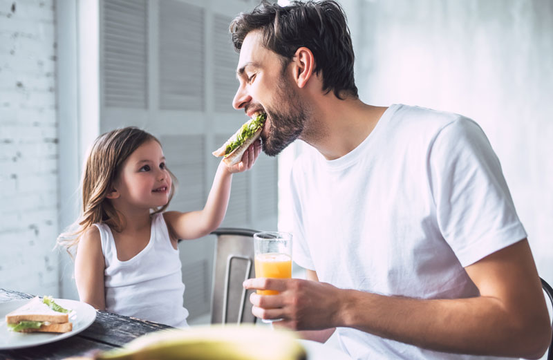 young girl giving dad a bite of her sandwich