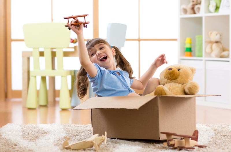 young girl sitting in a box and flying a plane
