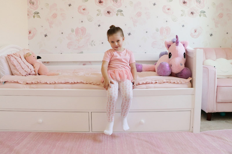 young girl sitting on a white toddler bed in a pink decorated room