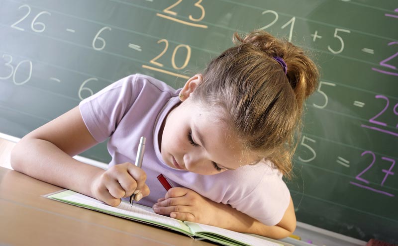 young girl writing in a book while sitting in front of a chalkboard