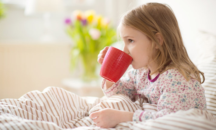 young sick girl drinking from cup while in bed